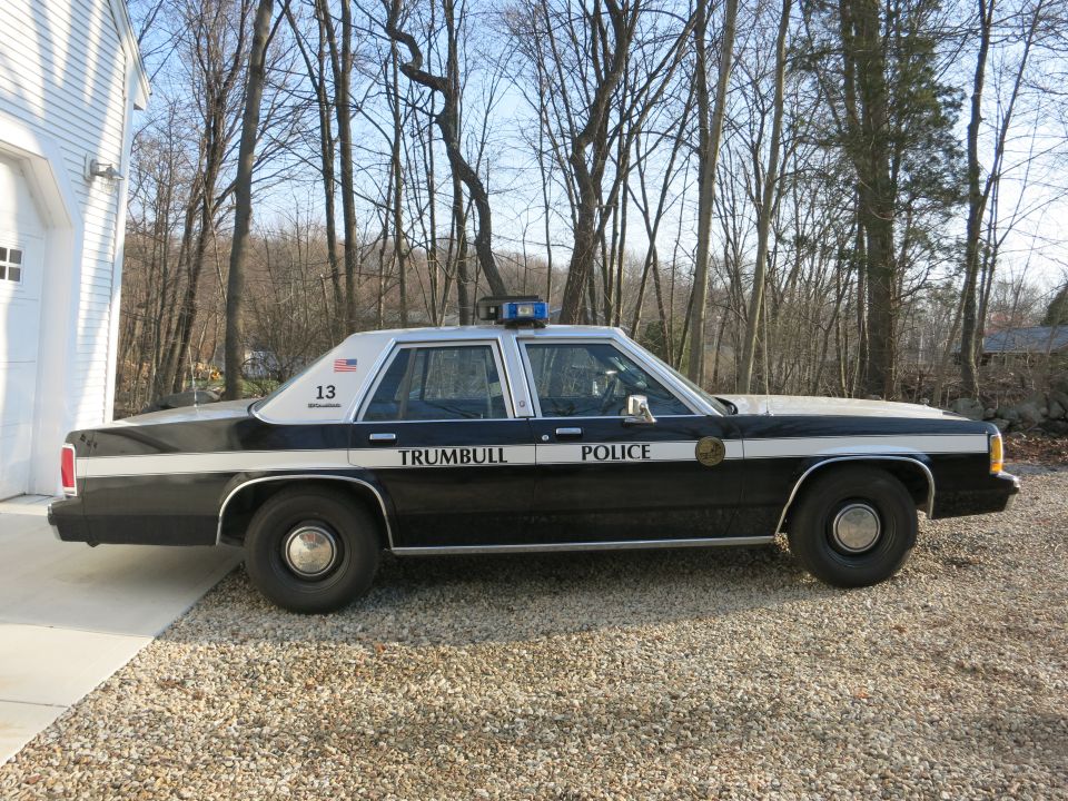 Side view of a black and white Trumbull Police Ford sedan on gravel