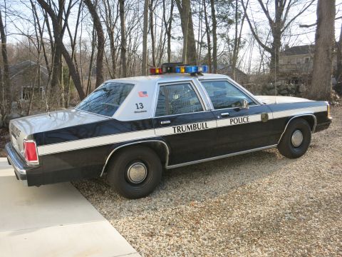 1991 Ford LTD Crown Victoria - Rear three-quarter view of a black-and-white Trumbull Police sedan, unit 13, with prisoner-cage rear windows, on a paved driveway.