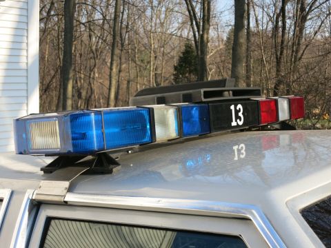 1991 Ford LTD Crown Victoria - Close-up of a police cruiser rooftop lightbar numbered 13 with blue, clear, and red lenses on a silver roof.
