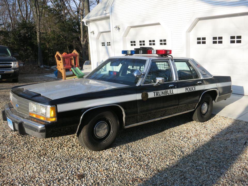Front view of a Trumbull Police Ford cruiser parked before two white garages