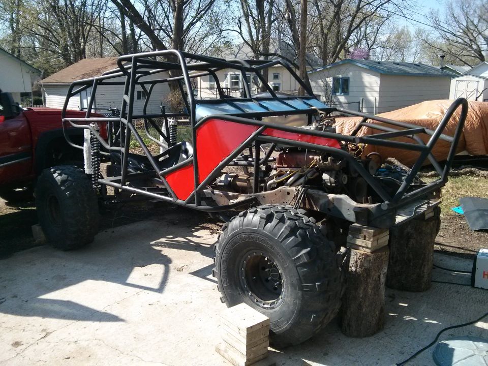 Custom buggy frame with red panels and large off-road tires, on blocks