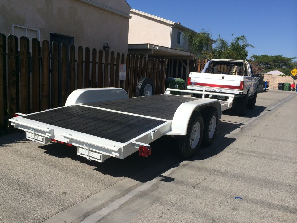 White pickup truck towing a white car trailer down a street