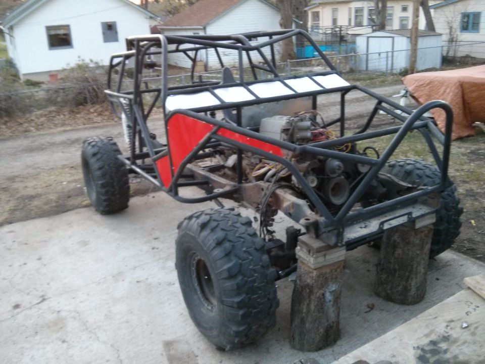 Custom buggy frame with large tires, engine visible, and red side panels. Vehicle is on blocks