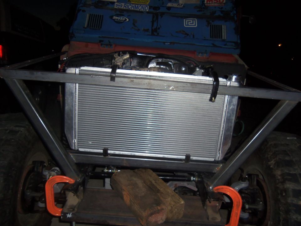 Custom off-road vehicle front end showing a large aluminum radiator mounted within a metal frame. Two wooden blocks are visible below the radiator