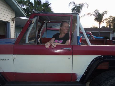 1968 Ford Bronco - A woman smiles from the driver's seat of a two-tone red and white vehicle, with another car in the background.