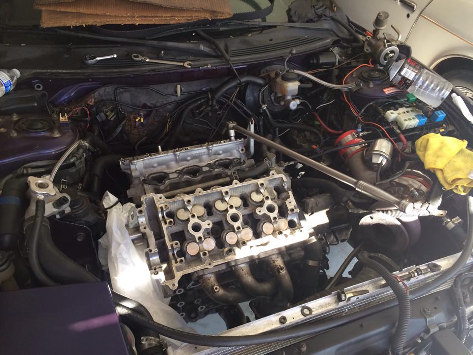 Engine bay with cylinder head removed, showing pistons and valves. Tools and parts are scattered around