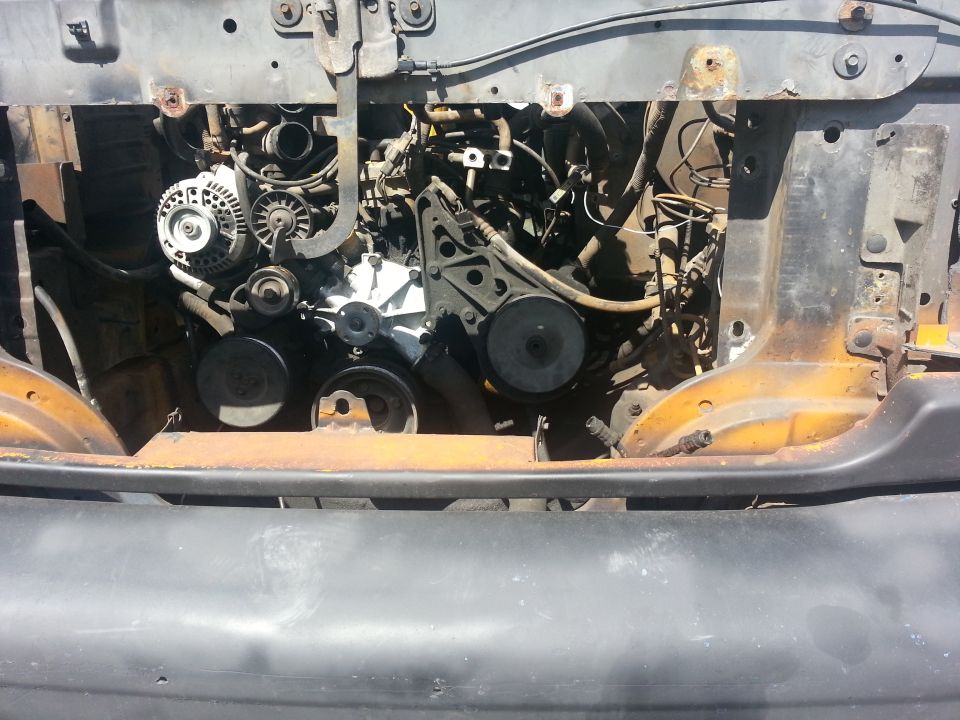 1994 Ford Bronco engine bay with visible alternator and pulleys, showing rust on the frame
