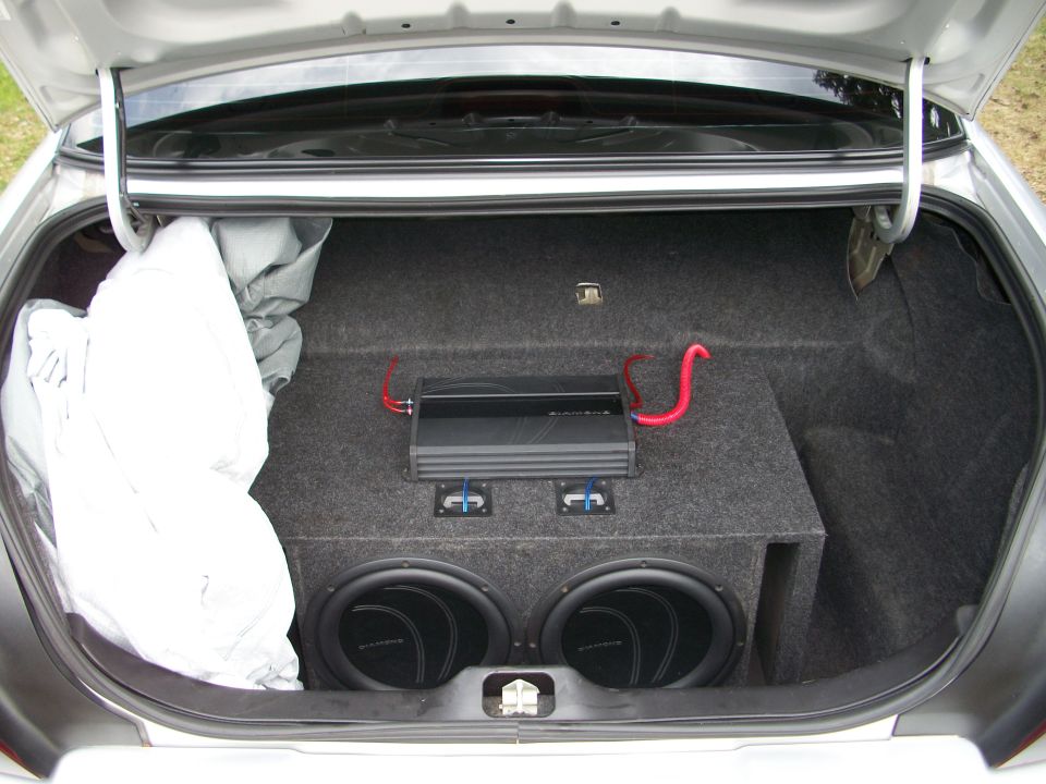 car trunk with dual subwoofers, amplifier, and a covered item on the left