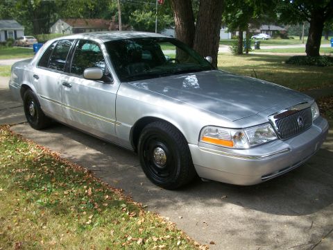 2003 Mercury Grand Marquis - A silver 2003 Mercury Grand Marquis is parked on a concrete driveway with trees and houses in the background.