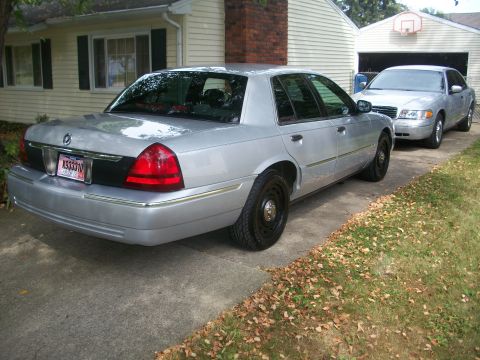 2003 Mercury Grand Marquis - Rear view of a silver 2003 Mercury Grand Marquis parked in a driveway next to another car.