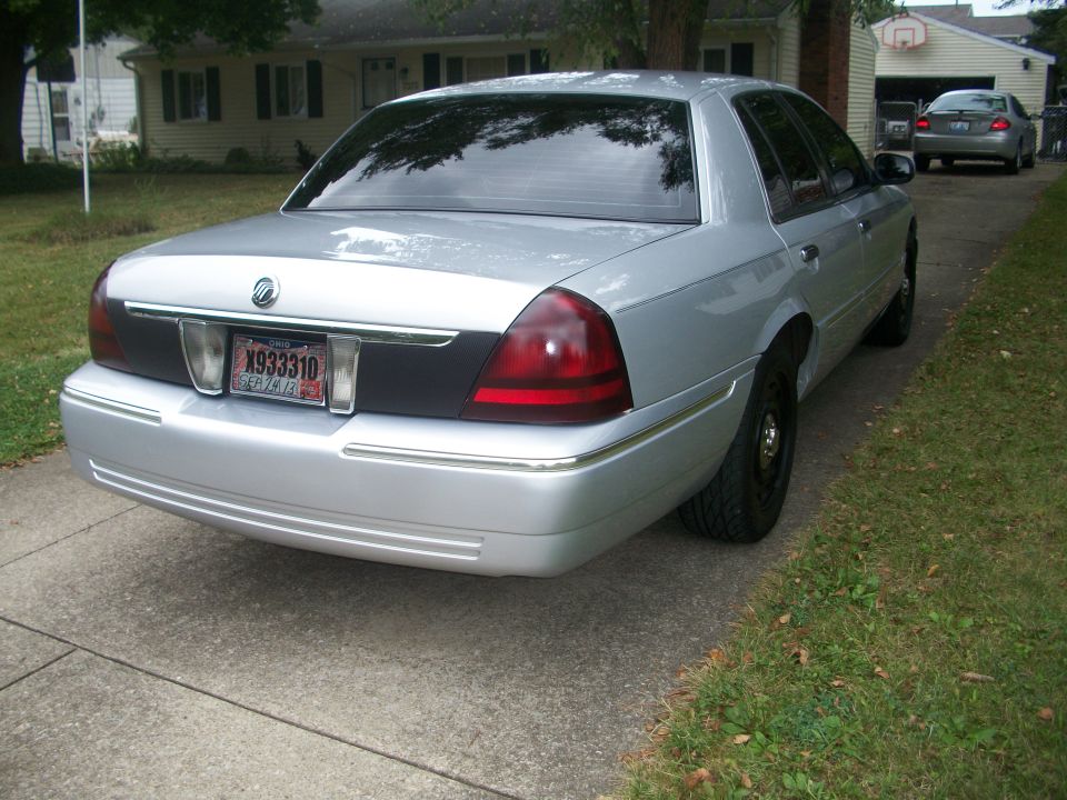 Rear view of a silver 2003 Mercury Grand Marquis parked in a driveway. Another car is visible in the background