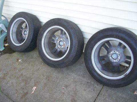 2003 Mercury Grand Marquis - Three car wheels and tires are shown leaning against a white wall.