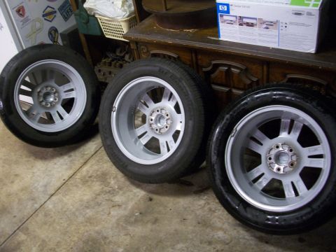2003 Mercury Grand Marquis - Three alloy wheels and tires are shown in a garage setting.
