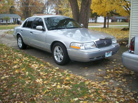 2003 Mercury Grand Marquis - A silver 2003 Mercury Grand Marquis is parked on a driveway, with another vehicle partially visible to the right.
