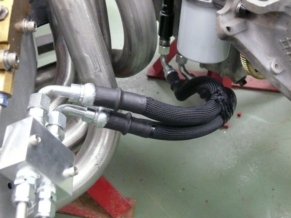 Engine part with braided hoses connected to a metal block, near exhaust pipes