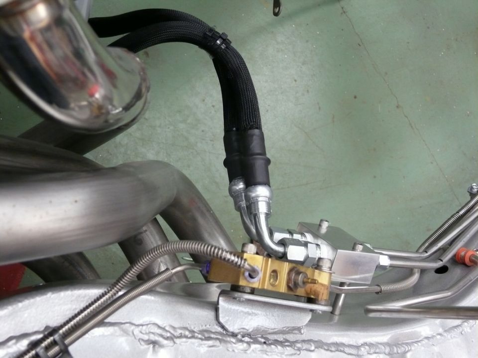 Exhaust manifold pipes and braided fuel lines connected to a brass fitting