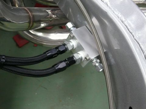 Engine oil cooler lines connected to a metal block, with exhaust pipes visible