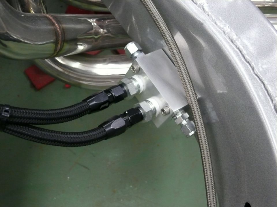 Engine oil cooler lines connected to a metal block, with exhaust pipes visible