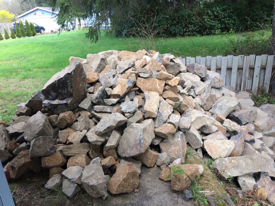 Pile of rocks in a yard with a wooden fence and grass in the background