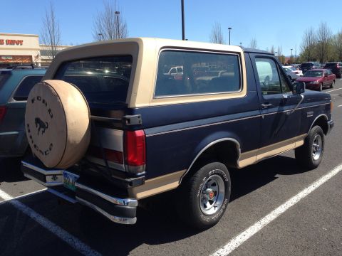 1990 Ford Bronco - Rear view of a 1990 Ford Bronco parked in a lot. Spare tire is mounted on the tailgate.