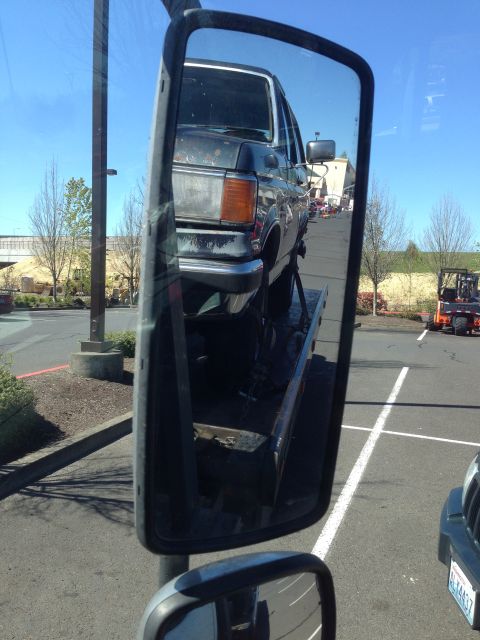 1990 Ford Bronco - A dark blue Ford Bronco is loaded onto a tow truck, viewed from the side mirror.