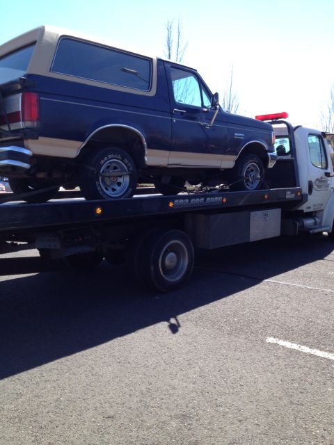 1990 Ford Bronco - A Ford Bronco is loaded onto a tow truck, its two-tone paint job visible.