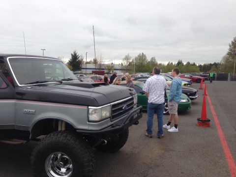 1989 Ford Bronco - A lifted Ford Bronco is parked at an outdoor event with other vehicles and people milling around.