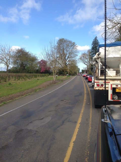 1989 Ford Bronco - A cement truck is part of a line of vehicles on a road with potholes under a partly cloudy sky.