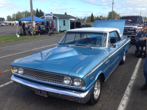 1989 Ford Bronco - A blue 1963 Ford Falcon Futura coupe is parked next to a pickup truck at an outdoor event.