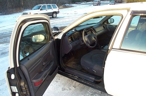 1991 Ford Crown Victoria LTD - The interior of a white police car is visible with the driver's side door open, revealing the dashboard and front seat.