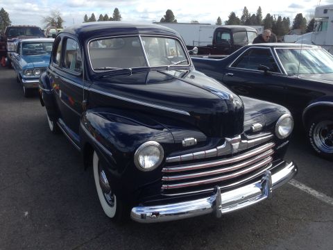 1989 Ford Bronco - A vintage dark blue sedan with a distinctive chrome grille is parked outdoors next to other vehicles.