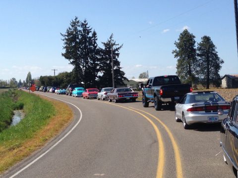 1989 Ford Bronco - A procession of vehicles, including a silver Ford Probe and a black pickup truck, travels down a two-lane road on a sunny day.