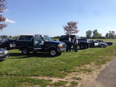 1989 Ford Bronco - Several vehicles are parked on a grassy field under a clear blue sky.