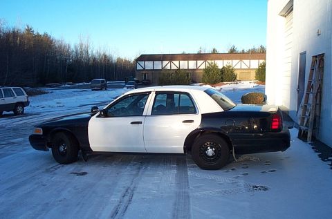 1991 Ford Crown Victoria LTD - A black and white police car is parked outside a building on a cold, snowy day.
