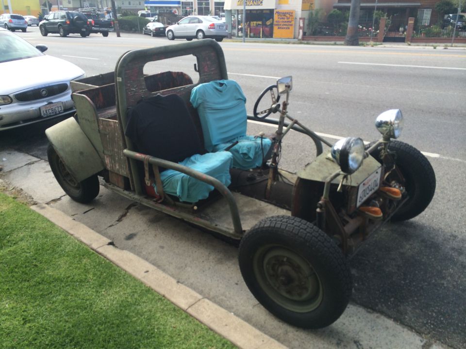 Custom open-air vehicle with wooden bed, two seats covered in blue fabric, and exposed frame