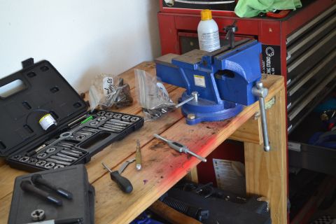 1981 Ford F-250 - A workbench is set up with a blue vise, a tap and die set, and various hardware, suggesting a repair or fabrication project.