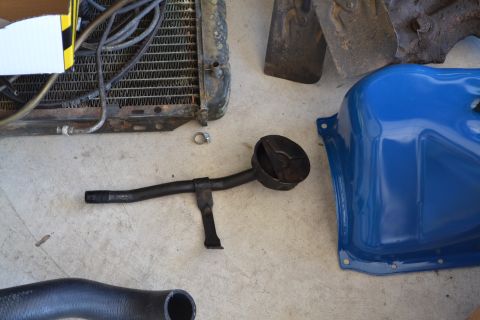 1981 Ford F-250 - Engine parts including an oil pan and pickup tube are laid out on a concrete surface.