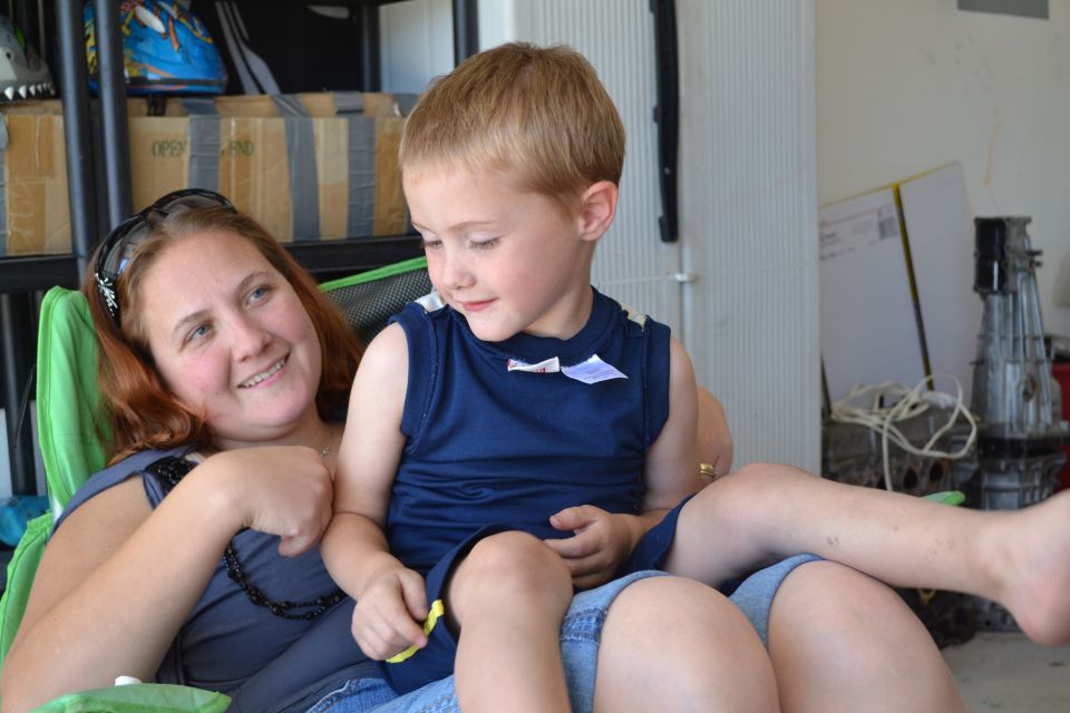 Woman and a young boy sitting together, with shelves and car parts in the background