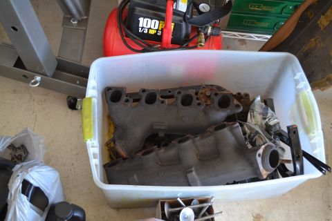 1981 Ford F-250 - Engine intake manifolds stored in a plastic bin with an air compressor in the background.
