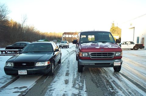 1991 Ford LTD Crown Victoria - Two Ford vehicles, a Crown Victoria and an Econoline van, sit on a snow-covered road in front of a building.