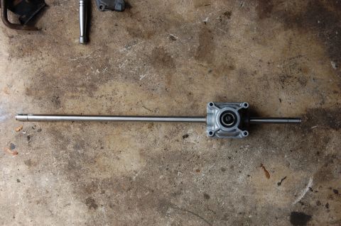 2006 Honda RANCHER - A drivetrain component rests on a textured concrete floor, with other metal parts visible in the background.