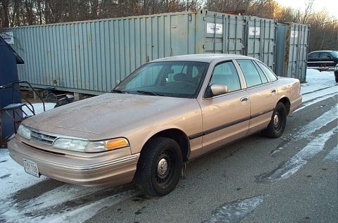 1991 Ford LTD Crown Victoria - A tan sedan is parked outdoors next to large shipping containers, with another vehicle visible in the background.
