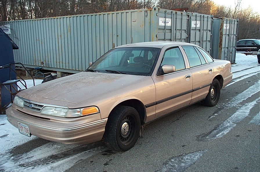 Tan sedan parked on asphalt with snow patches, showing front fender, hood, and side