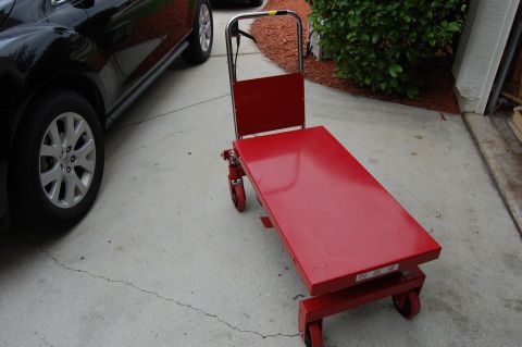 2006 Honda RANCHER - A red hydraulic lift table is shown next to a black car, parked on a concrete driveway.