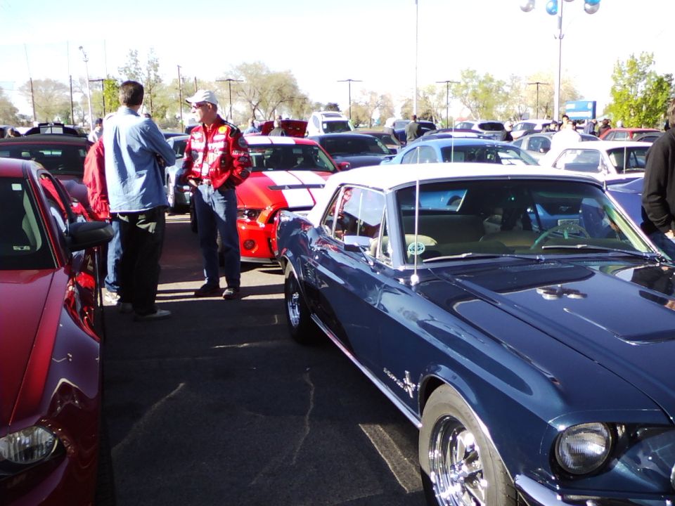Blue convertible Mustang with a white top, parked in a lot with other cars and people