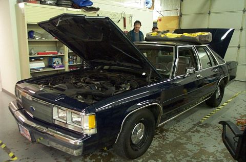 1991 Ford LTD Crown Victoria - A dark blue sedan, likely from the early 1990s, is parked indoors with its hood open.