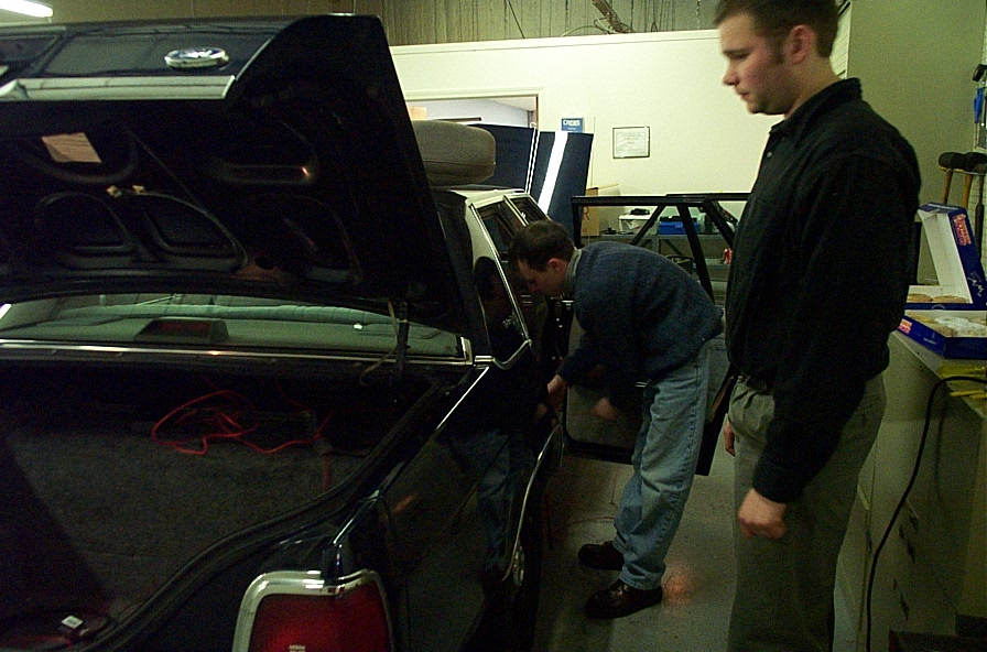 Two guys working on the trunk and interior of a dark sedan