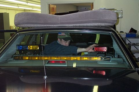 1991 Ford LTD Crown Victoria - A person installs emergency lights inside a dark colored car, viewed through the rear window.