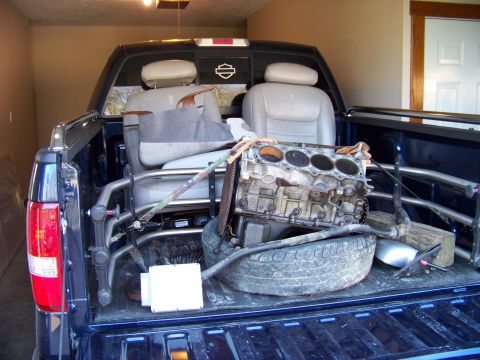 1999 Mercury Grand Marquis - Engine block and spare tire are loaded into the bed of a blue pickup truck.