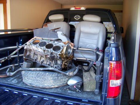 1999 Mercury Grand Marquis - Engine block and seats are loaded into the bed of a pickup truck, which is parked inside a garage.